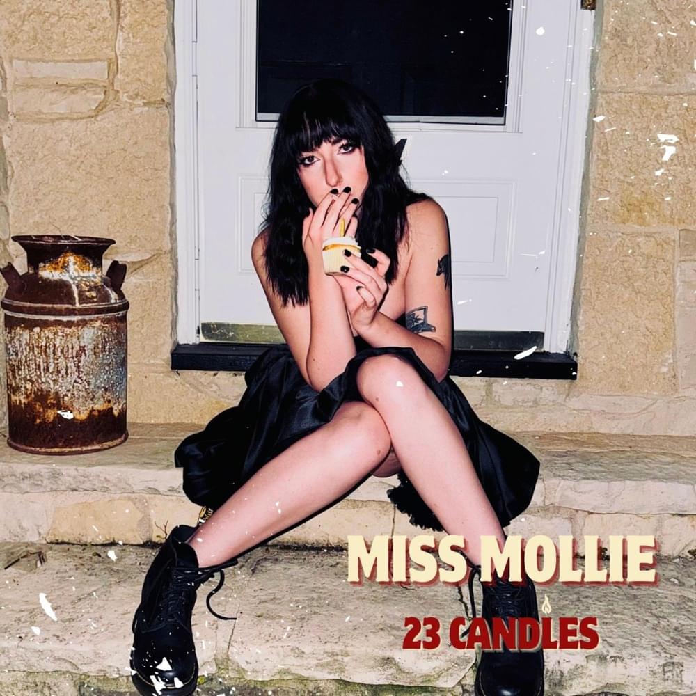 A woman with black hair sits on stone steps in front of a white door, holding a cupcake. She wears a black dress and boots. Text reads: Miss Mollie Cule Mega Dose Psychedelic Tablets (4ct) | 5000mg—ideal for microdosing fans.